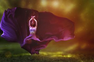 A person in a flowing purple dress is captured mid-dance, with arms raised above the head and the dress billowing dramatically around the body. The background is a blend of warm colors, creating a mystical and ethereal atmosphere.
