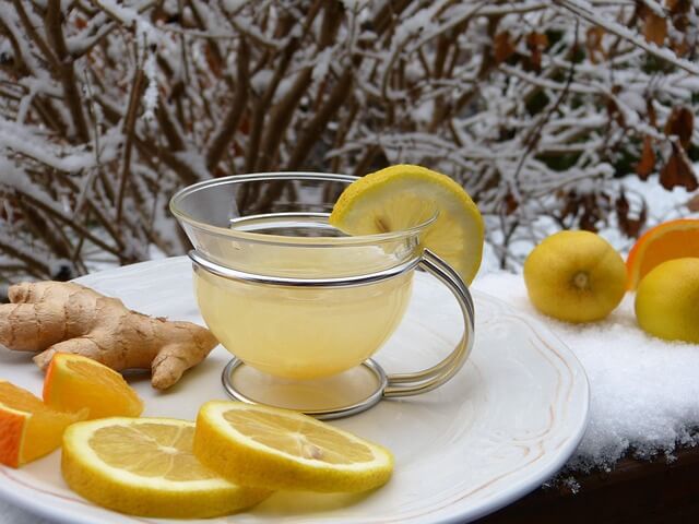 Glass cup of lemon ginger tea with citrus slices and fresh ginger on a white plate, set against a snowy outdoor background.