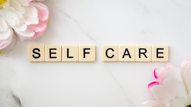 Scrabble-style tiles spelling “SELF CARE” on a white marble surface, surrounded by soft pink and white flowers.